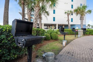 Ein Grillbereich im Freien mit einem gepflasterten Weg, Palmen und einem Gebäude im Hintergrund.