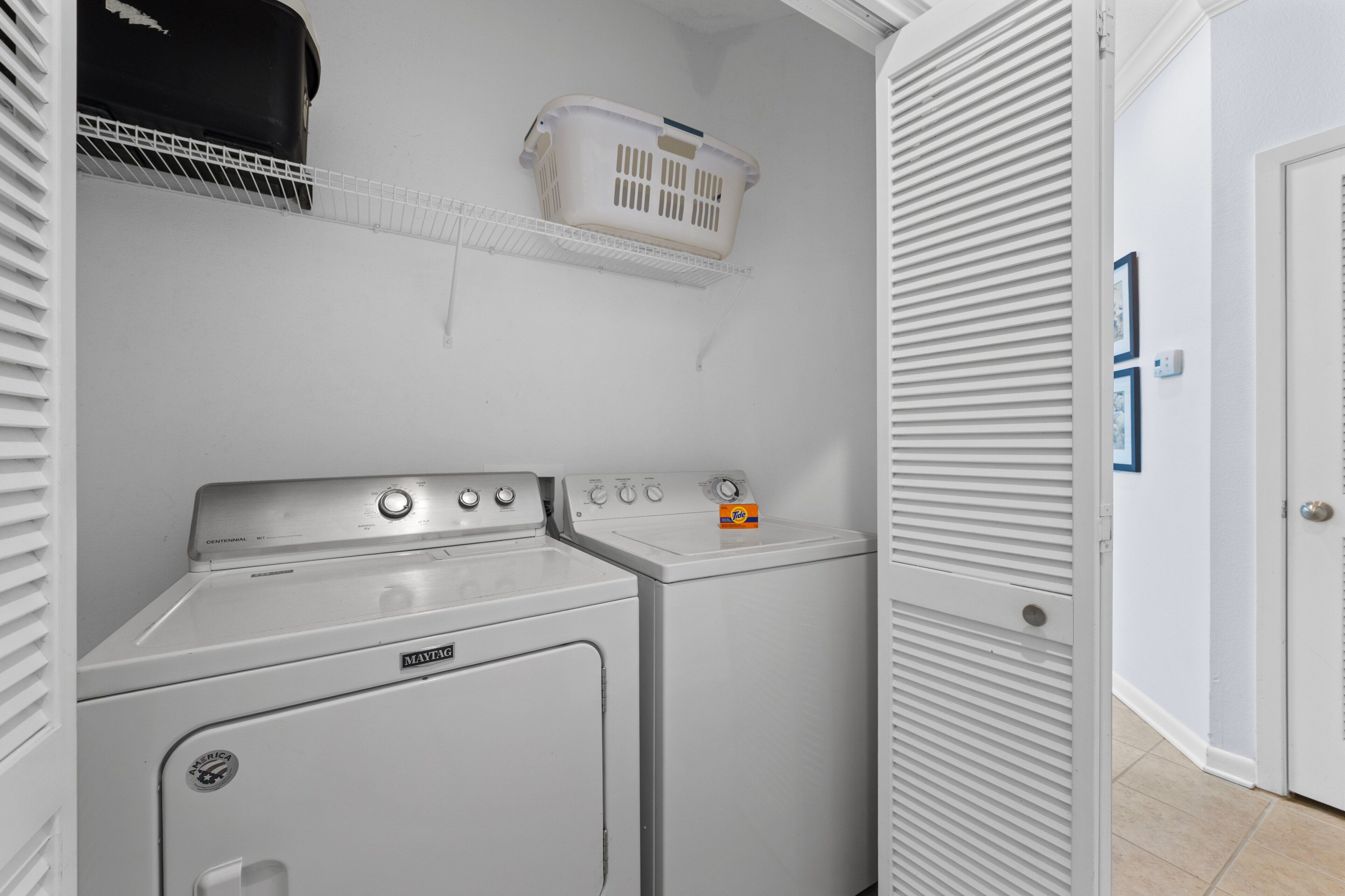 A laundry room with two front-loading washers and dryers, a white basket on a shelf, and a door with a lock.