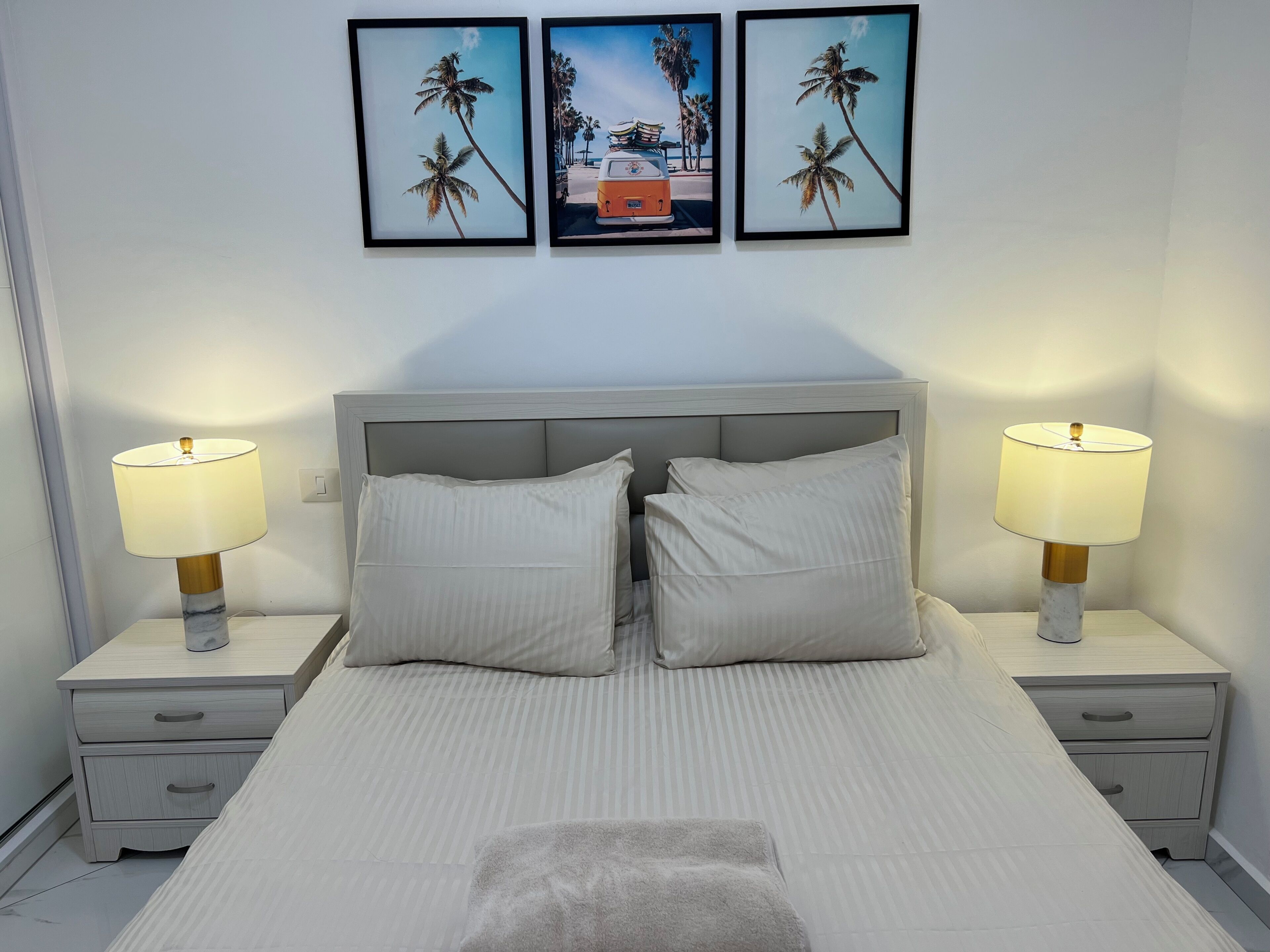 A neatly made bed with two pillows, two bedside lamps, and a nightstand with a drawer.