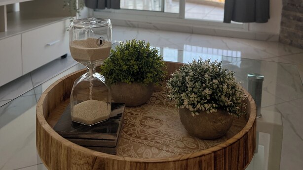 Un salon moderne doté d’une grande fenêtre, d’une table basse ronde en bois agrémentée d’objets décoratifs, d’un téléviseur placé à gauche et d’un balcon offrant une vue sur la mer.