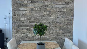 A dining table with four woven placemats, a potted plant, and a stone wall with a light fixture.