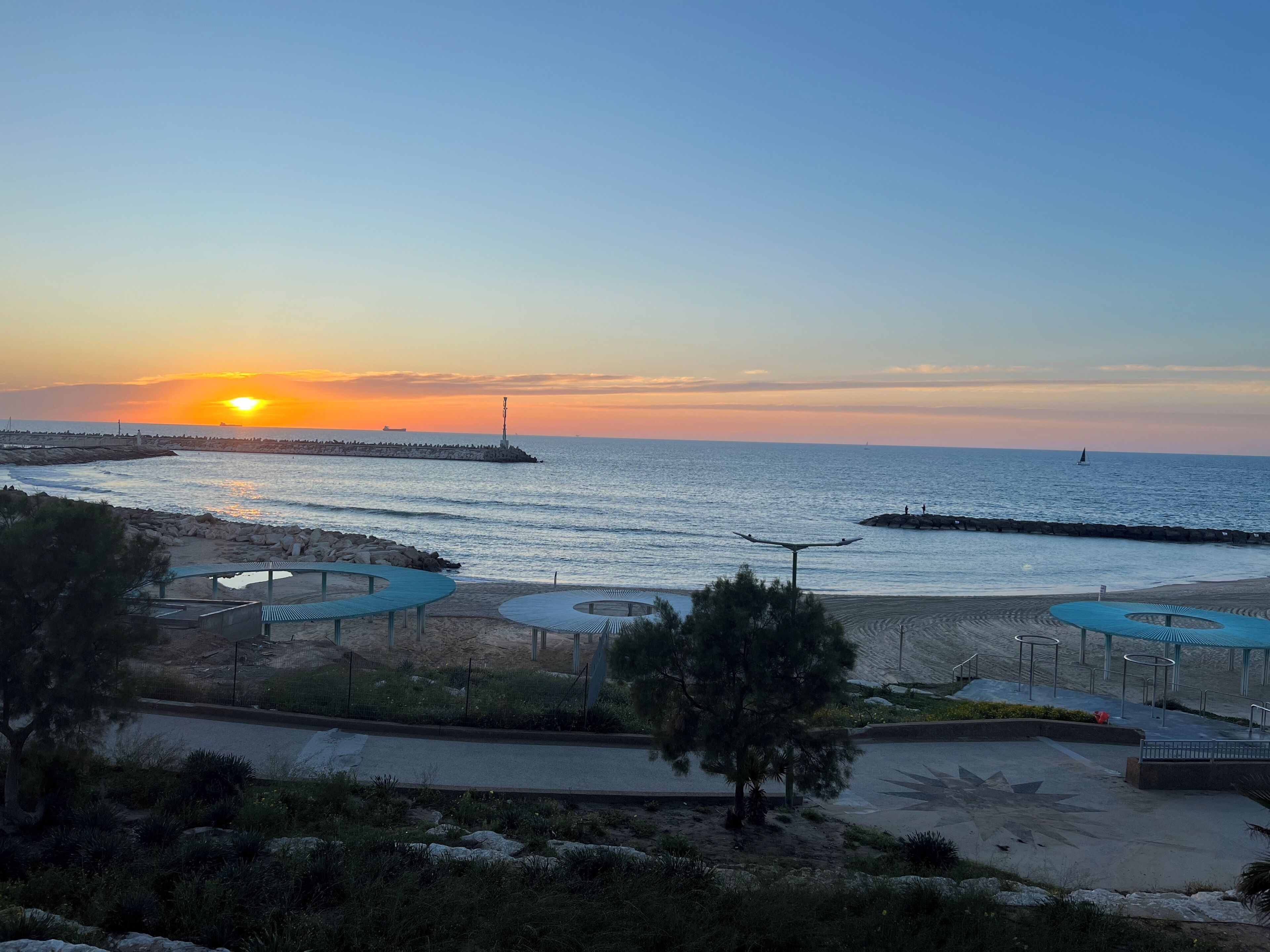 Een kustzonsondergang met een steiger, strandzitplaatsen en een ster-vormig voetpad.