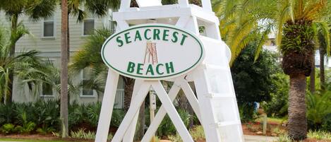 Señal de Seacrest Beach con una silla blanca y una palmera al fondo.