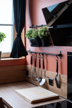 Une cuisine dotée d’un plan de travail en bois, d’ustensiles suspendus et de plantes en pot disposées sur une étagère fixée au mur.