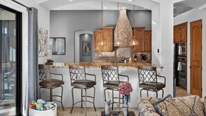 A modern kitchen with a central island, bar stools, pendant lighting, and wooden cabinetry.