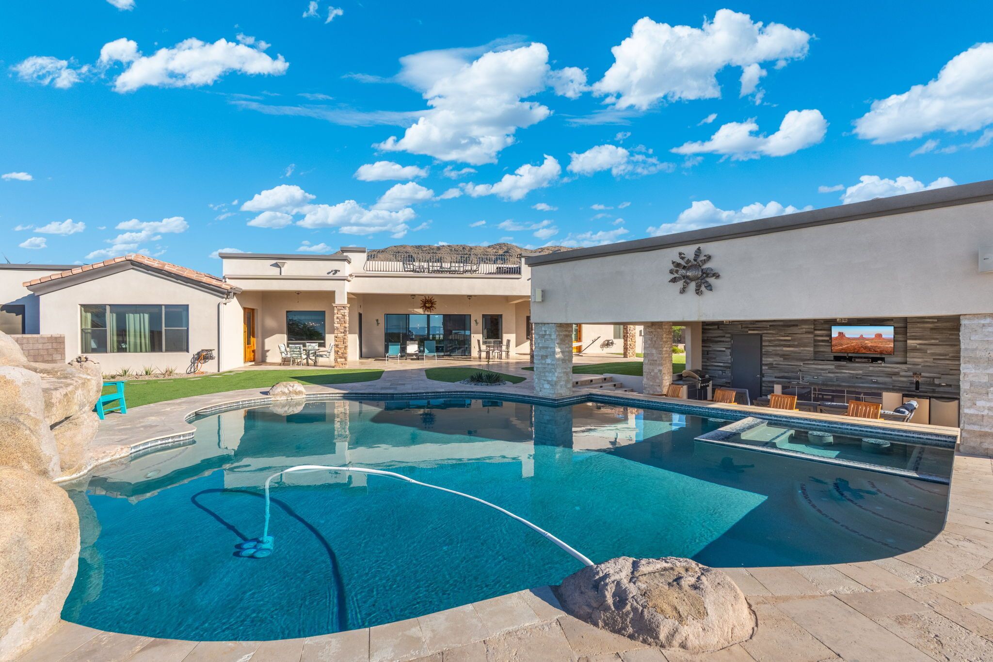 Une maison moderne dotée d’une piscine, d’un espace salon extérieur et d’un grand écran de télévision.