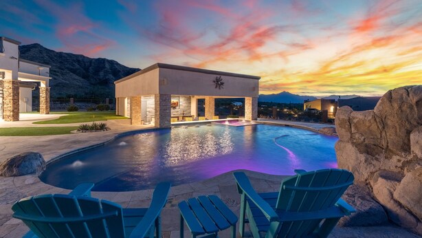 A modern building with a pool, green chairs, and a mountainous backdrop.
