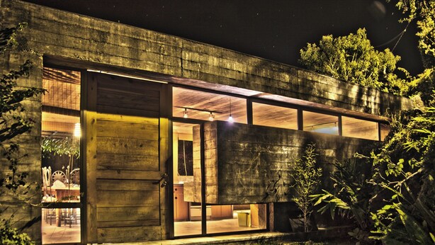 A modern building with large windows, a wooden door, and a visible interior with a dining area.