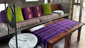 A room with a concrete ceiling, a sofa with colorful cushions, a wooden table, and a chair.