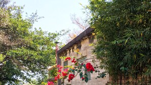 A narrow alleyway with a stone wall on one side and a building with a tiled roof on the other.