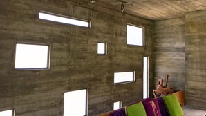A room with a concrete ceiling, multiple windows, and a wooden chair with cushions.