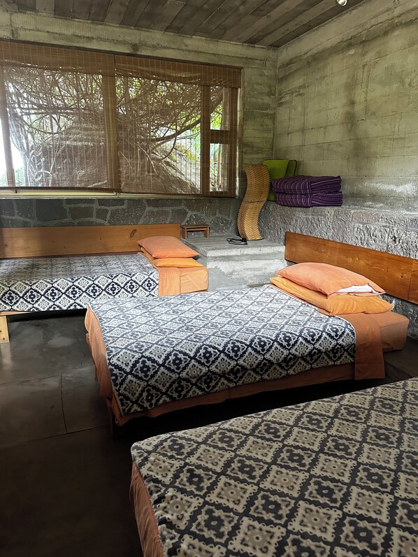 A room with two beds, a small table, and a window with a view of trees.