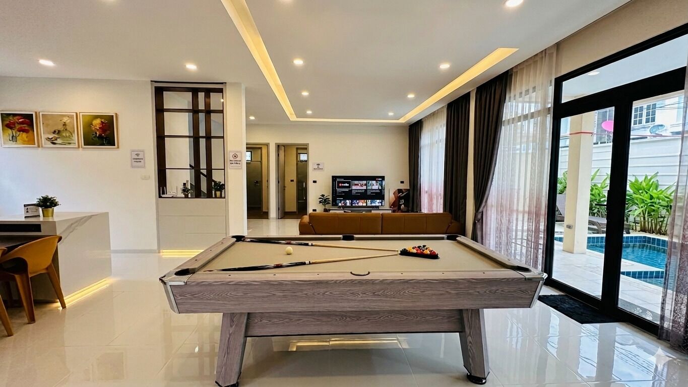A pool table in a modern room with a TV, a sofa, and a view of a swimming pool.