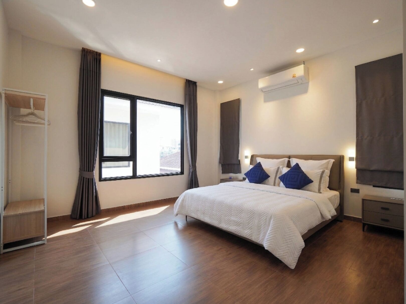 A modern hotel room with a large bed, a wardrobe, a window with curtains, and an air conditioning unit.