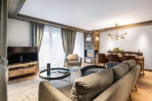 A modern living room with a television, sofa, dining table, and fireplace. - Wifi, 100m from resort center, 2nd floor, fitness, swimming pool, sauna, hammam, balcony, tv (Les Gets)
