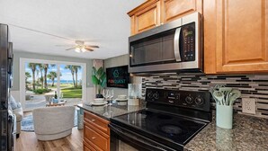 A modern kitchen with a microwave, stove, and wooden cabinets. - The Summit 131 - Ground Floor Beachfront! Walk to Sand! (Panama City Beach)