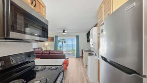 A kitchen with a stove, microwave, and refrigerator, a dining area with a table and chairs, and a view of the outdoors. - The Summit 206 - 2nd floor - Includes Seasonal  Beach Chairs (Panama City Beach)