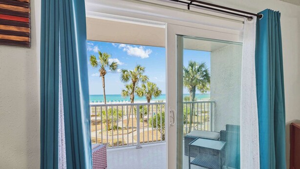 A balcony with a glass door, a view of the beach, and a table with chairs. - The Summit 206 - 2nd floor - Includes Seasonal  Beach Chairs (Panama City Beach)