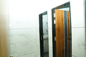 A bathroom with white marble tiles, a wooden door, and a visible sink.