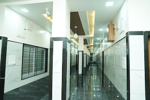 A corridor with marble flooring, a security camera, and a window with metal bars. - Hotel Shriram Nivas Lodging (Hingoli)