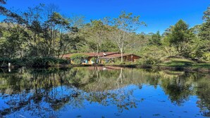 Una casa accanto a un lago tranquillo, circondata da alberi, con cielo sereno e un'antenna parabolica visibile.