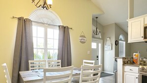Ein Essbereich mit Tisch und Stühlen, eine Küche mit Mikrowelle und Herd sowie ein Fenster mit Vorhängen.