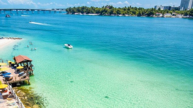 Um resort à beira-mar com águas turquesa cristalinas, um píer e uma fileira de espreguiçadeiras.