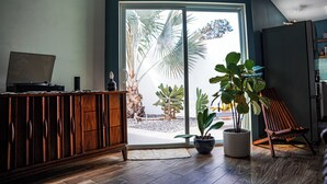 Quarto com armário de madeira, planta em vaso, cadeira e grande porta de vidro deslizante que dá para área externa com plantas.