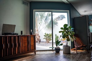 A room with a wooden cabinet, a potted plant, a chair, and a large sliding glass door leading to an outdoor area with plants. - Cozy Villa Near Clearwater Beach with Patio & Hammock (Clearwater)