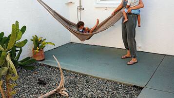 A hammock between two people, a potted plant, and a window.