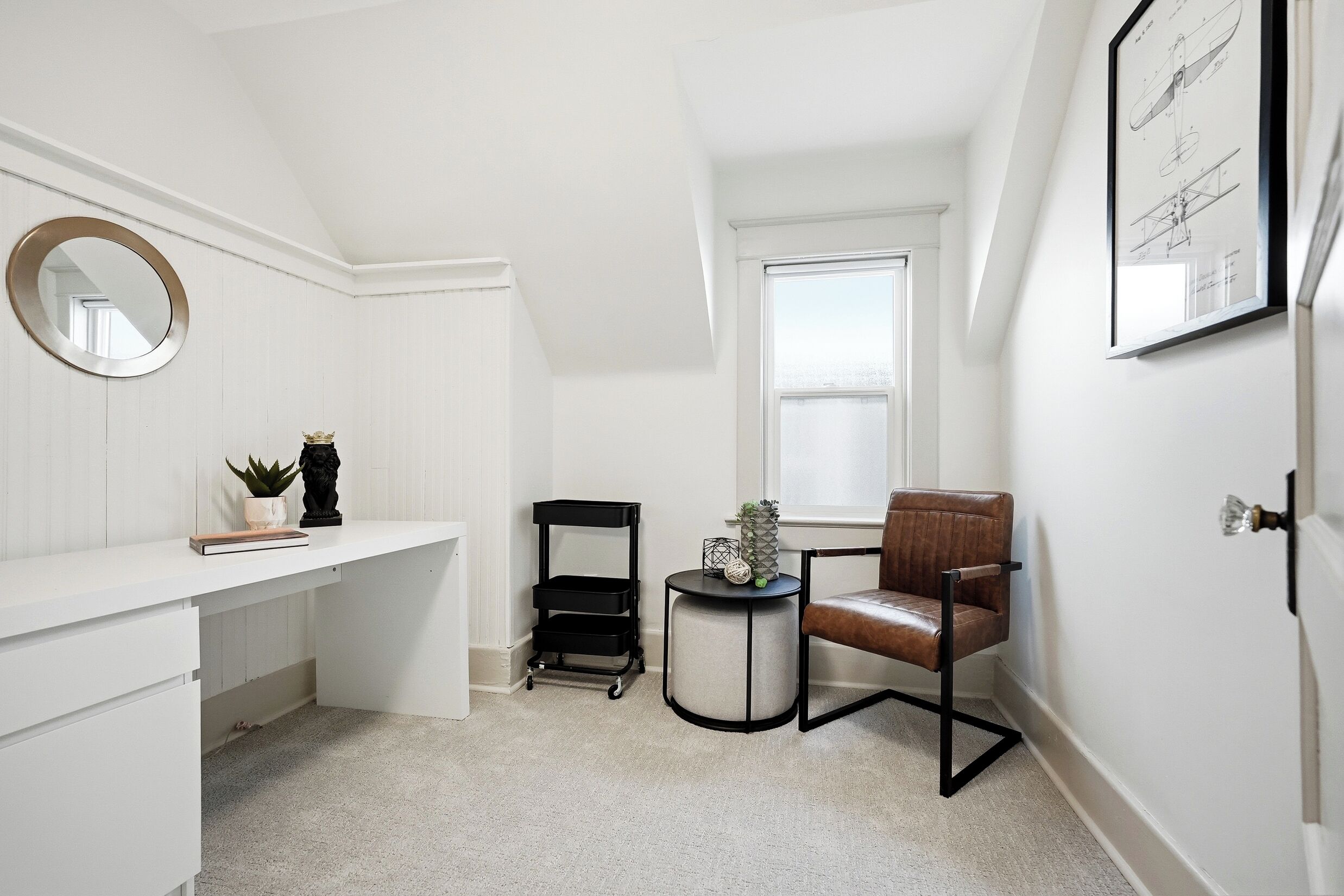Une pièce blanche comprenant un bureau, une chaise et une petite table ronde agrémentée d’objets décoratifs.