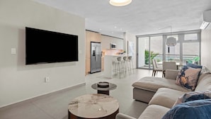 Una sala de estar moderna con un televisor de pantalla plana, una mesa redonda de centro, un sofá con cojines y un comedor con sillas.