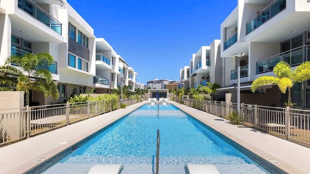 Un hotel moderno con piscina central, rodeado de balcones y un cielo azul despejado.