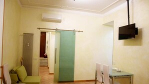A hotel room with a green sofa, a dining table with chairs, a TV mounted on the wall, and a sliding door. - Roman Holiday Home Re di Roma (Rome)