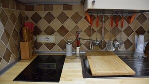 A kitchen with a black induction cooktop, a wooden cutting board, a sink, and hanging utensils. - Roman Holiday Home Re di Roma (Rome)