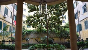 A courtyard with a central tree, surrounded by potted plants and a cobblestone path. - Roman Holiday Home Re di Roma (Rome)