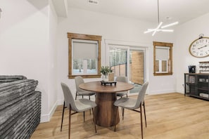 Un comedor con una mesa redonda de madera, cuatro sillas grises y un reloj en la pared.