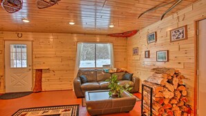 Ein gemütliches Blockhaus-Interieur mit einem Ledersofa, einem Couchtisch, einem Kamin und einem Holzstoß.