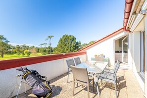 Un balcon avec une table et des chaises, un sac de golf et une vue sur un paysage verdoyant.