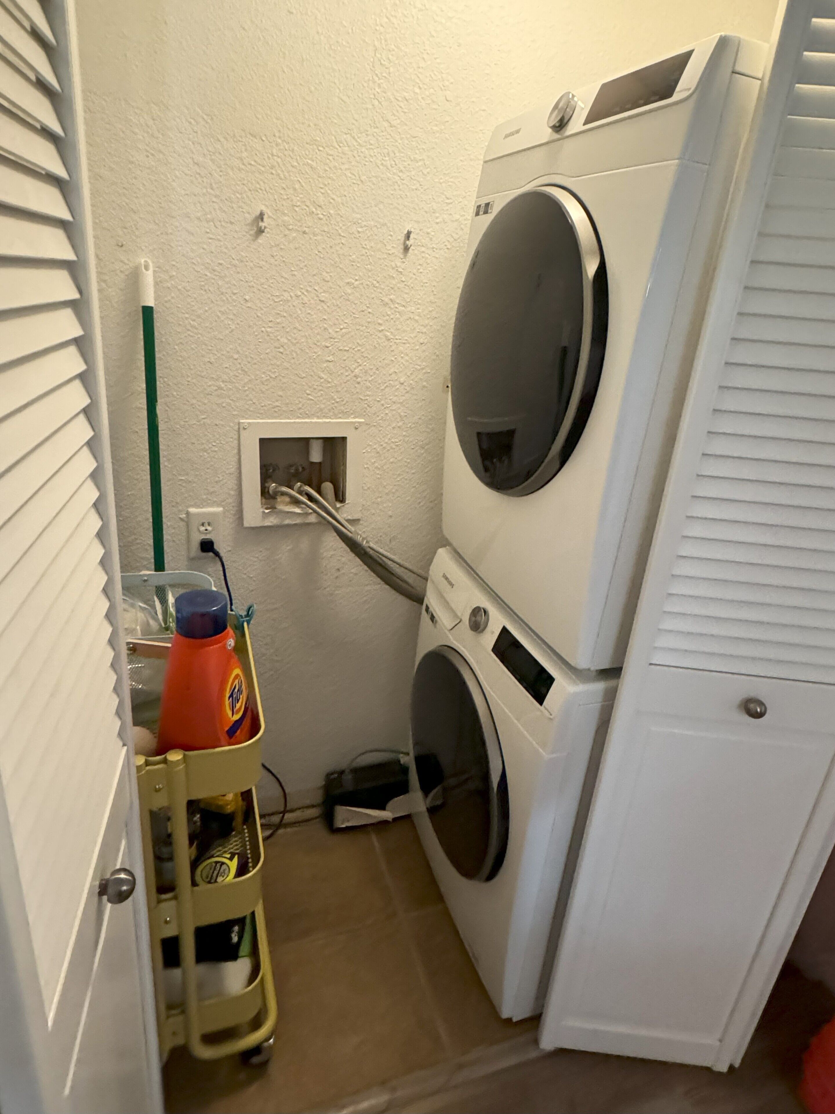 A laundry room with a washing machine, dryer, and a cart with cleaning supplies.
