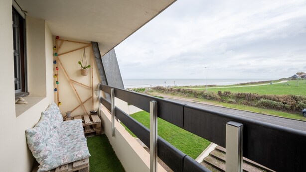 Ein Balkon mit Meerblick, einer Holzbank und einer hängenden Pflanze.