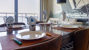 A dining area with a table set for four, a view of the sea through large windows, and a sailboat painting on the wall. - L'Étoile de Mer - Vue sur la Plage de Bray-Dunes (Bray-Dunes)