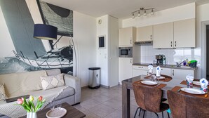 A modern living room with a sofa, coffee table, and a dining area with chairs and a table set for two. - L'Étoile de Mer - Vue sur la Plage de Bray-Dunes (Bray-Dunes)