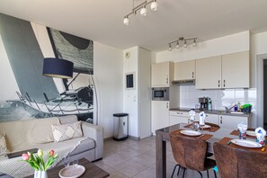 Ett modernt vardagsrum med en soffa, ett soffbord och en matplats med stolar och ett bord dukat för två personer.