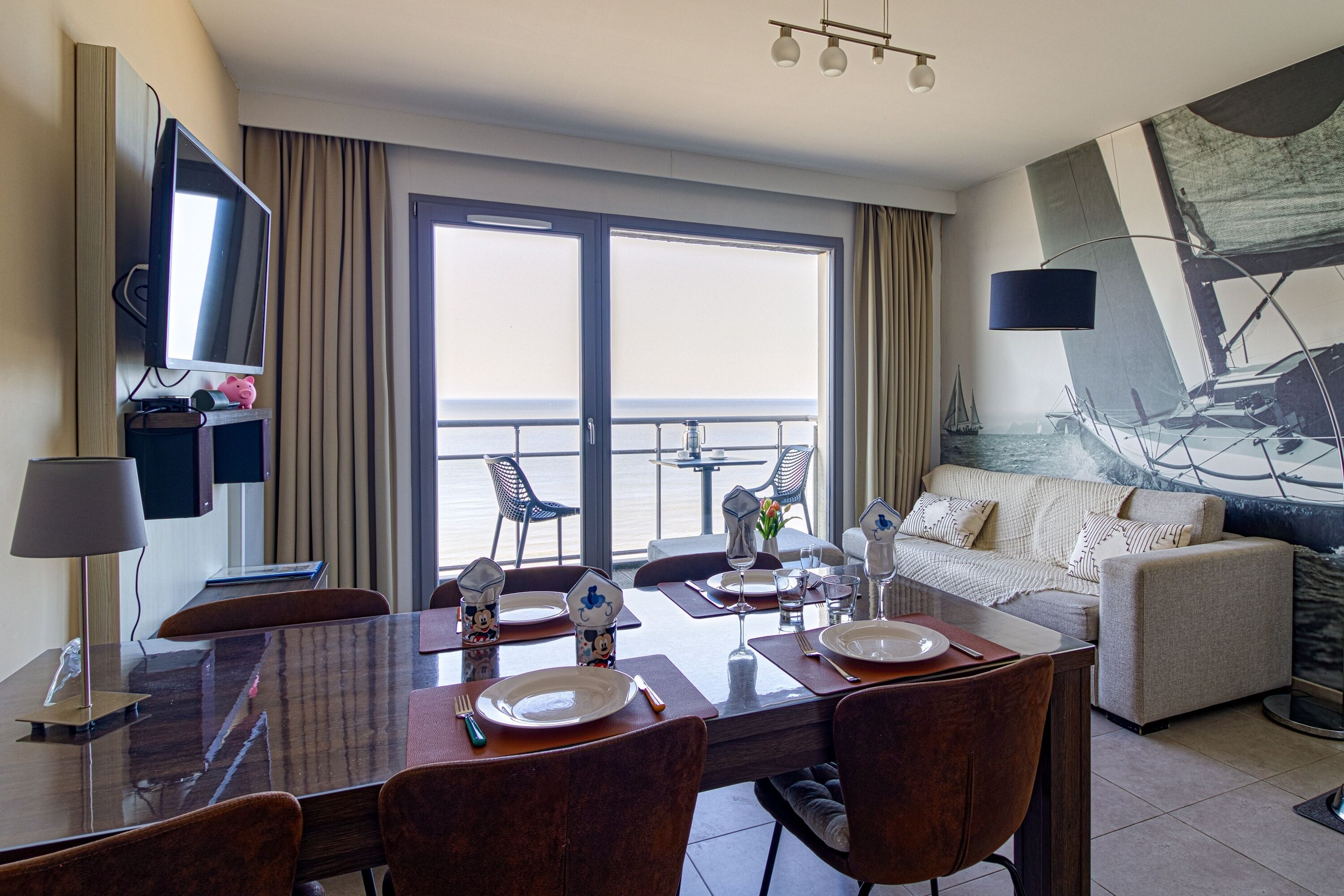 A hotel room with a dining area, a sofa, a TV, and a large window with a view.