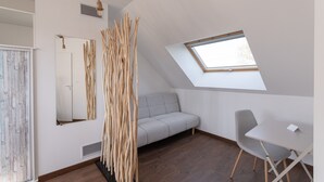 Um quarto com teto inclinado, um claraboia, um sofá, uma cadeira e um objeto decorativo de madeira.