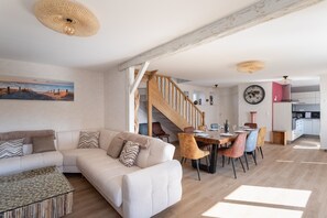 A modern living room with a sofa, dining table, chairs, and a staircase. - Au Clos du Magnolia - Grande maison pour 10 (Pléneuf-Val-André)