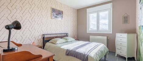 A bedroom with a bed, a desk, a chair, a radiator, a window, and a wall-mounted picture.