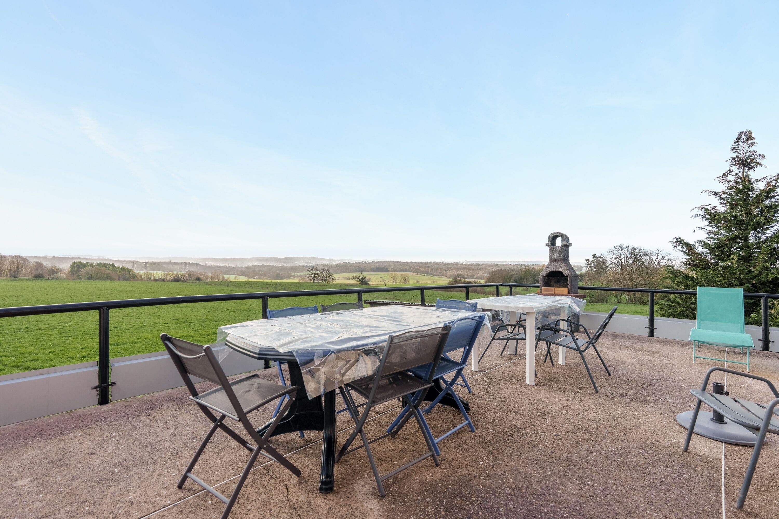 An outdoor patio with a table and chairs, a grill, and a view of the countryside.