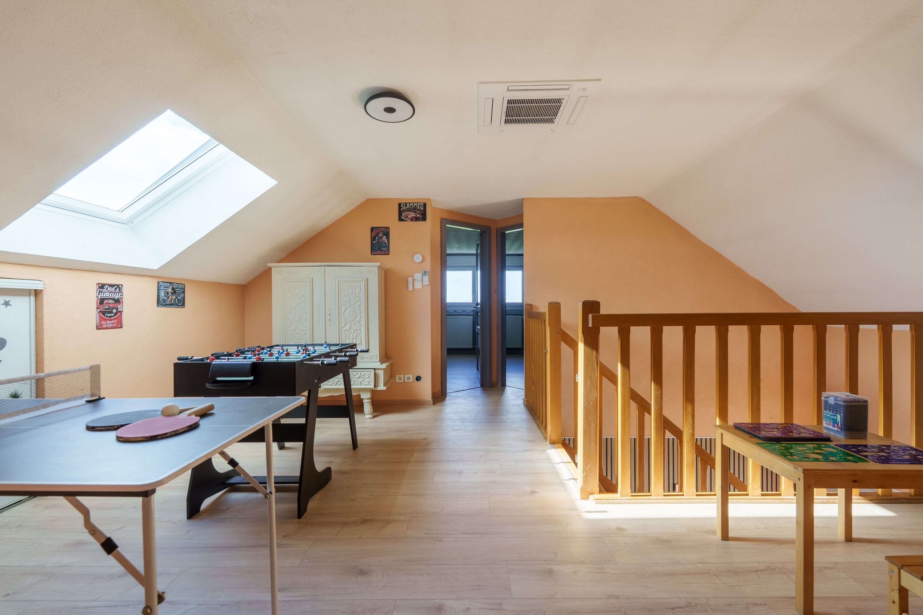 A room with a ping pong table, foosball table, and a wooden staircase.
